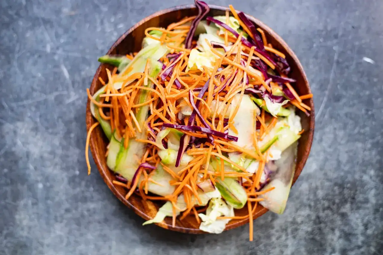 Salade de chou color&eacute;e avec carottes r&acirc;p&eacute;es, concombre et chou rouge dans un bol en bois.