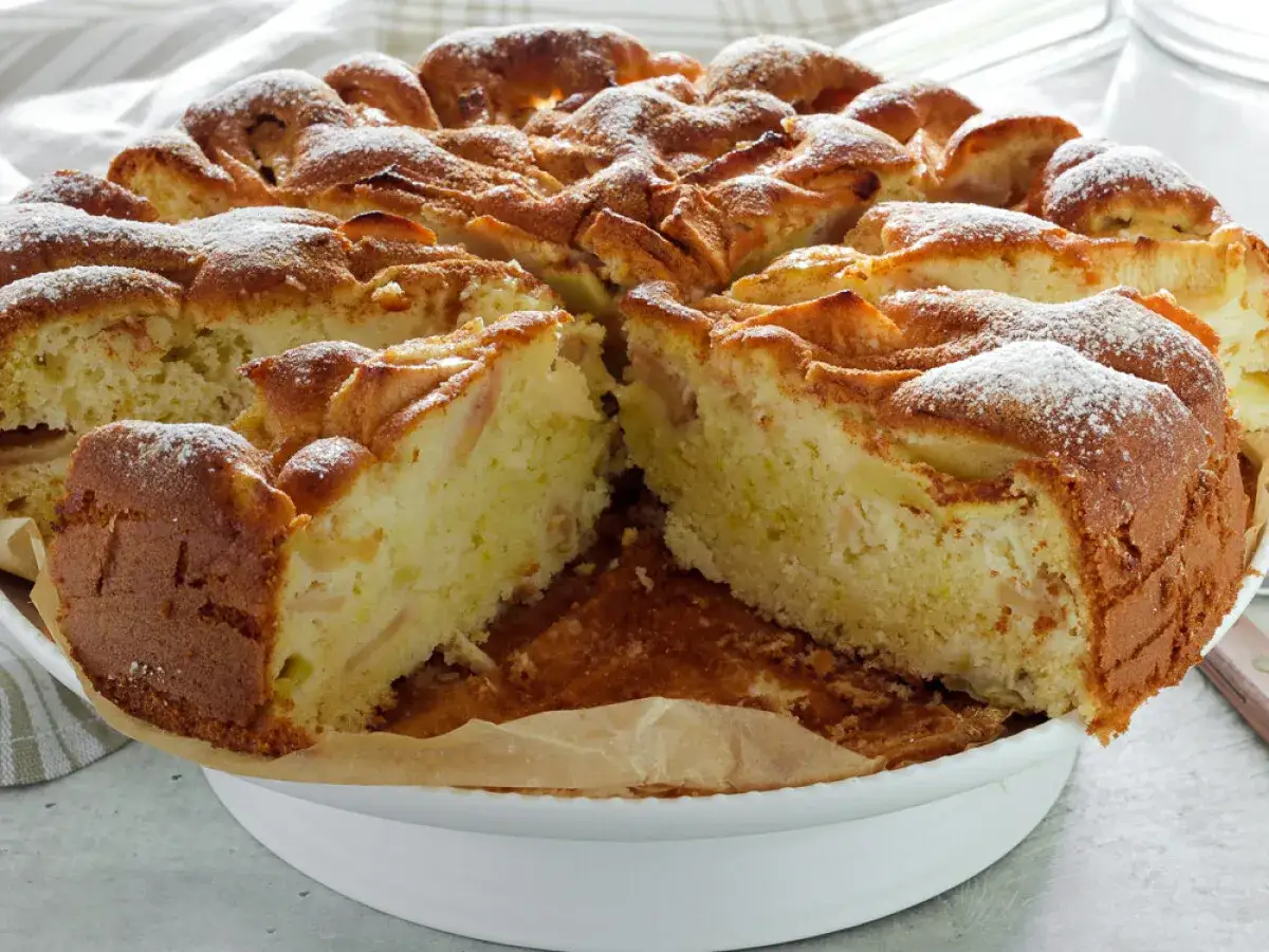 Puszyste ciasto z jabłkami, posypane cukrem pudrem, wygląda apetycznie. Idealne na podwieczorek.