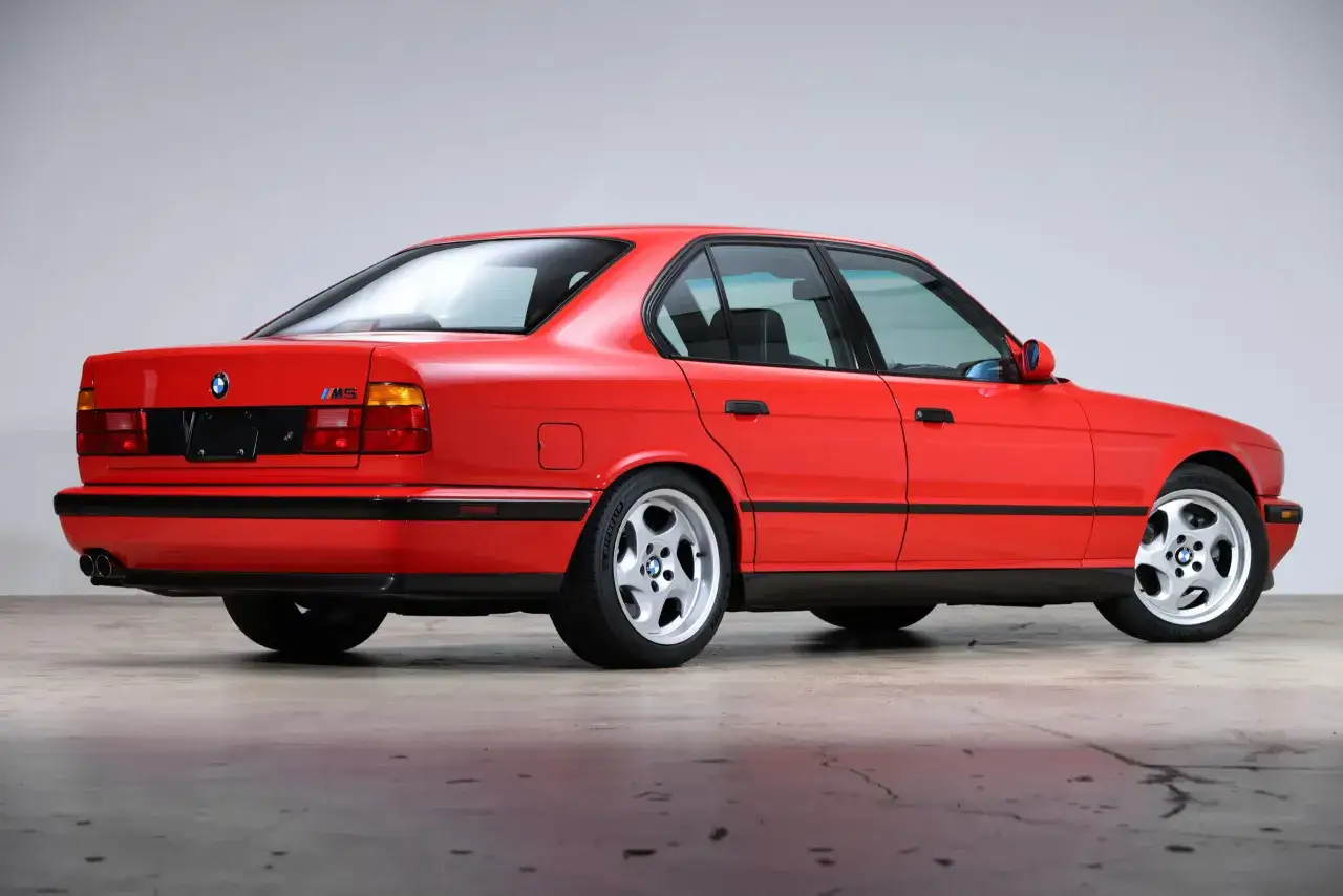 Czerwone BMW E34 M5 z lat 90. z charakterystycznymi felgami i podwójnymi końcówkami wydechu.