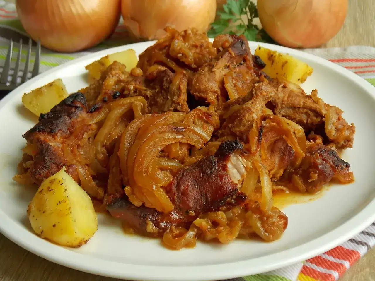Karkówka pieczona w plastrach z cebulą, podana z ziemniakami. Aromatyczne danie, które rozpływa się w ustach.