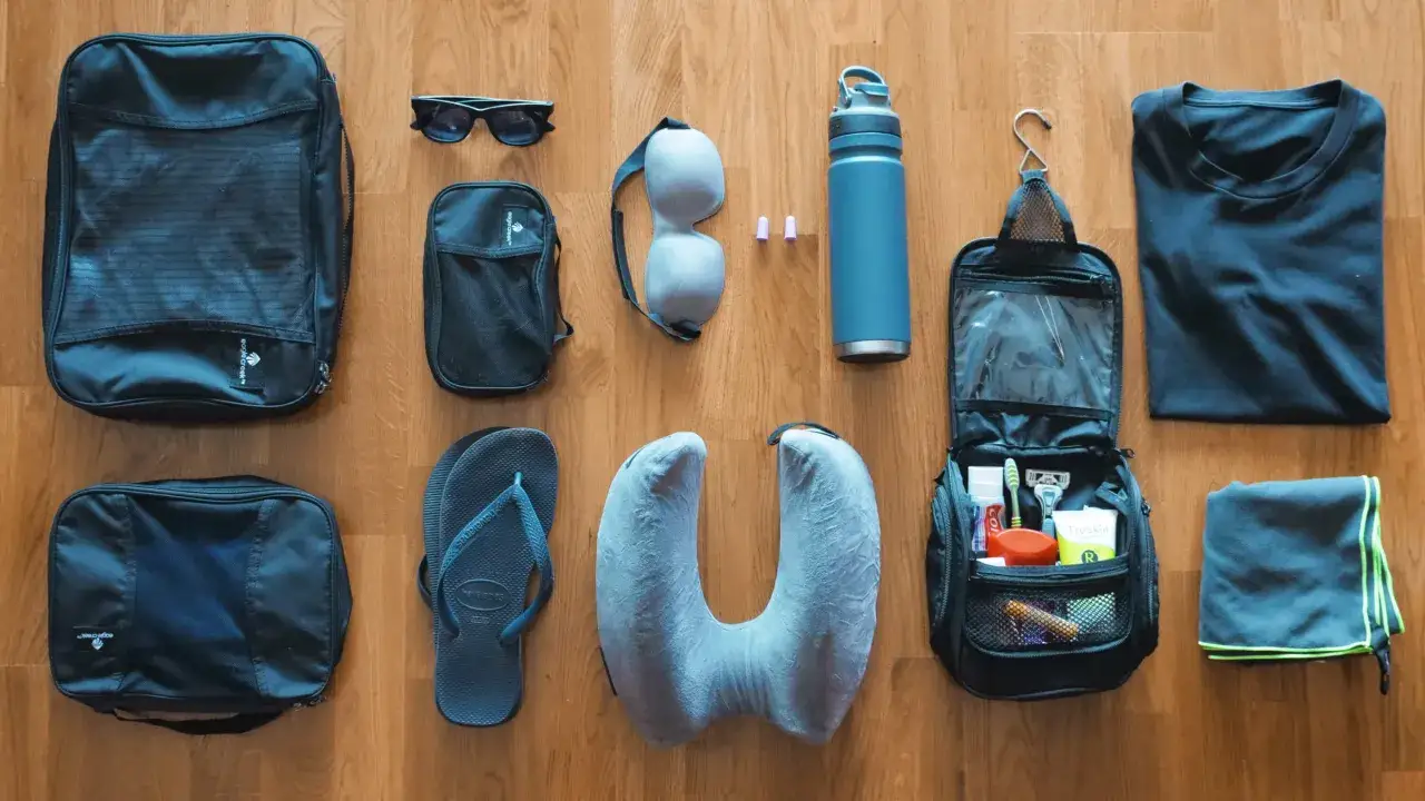 Lista de artículos esenciales para llevar a Tailandia: neceser, chanclas, almohada de viaje, gafas de sol, botella de agua, camiseta y toalla.