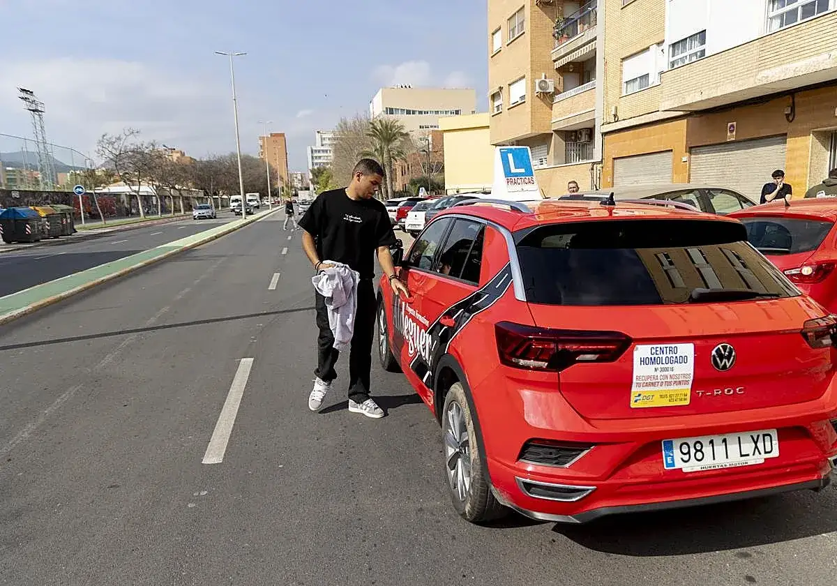 Joven se acerca a coche rojo de autoescuela. ¡Con 17 años ya se puede sacar el carnet de conducir!