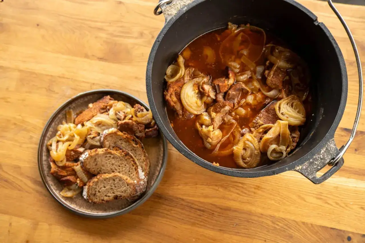 Herzhaftes Zwiebelfleisch im Dutch Oven, daneben eine Portion mit Brot.
