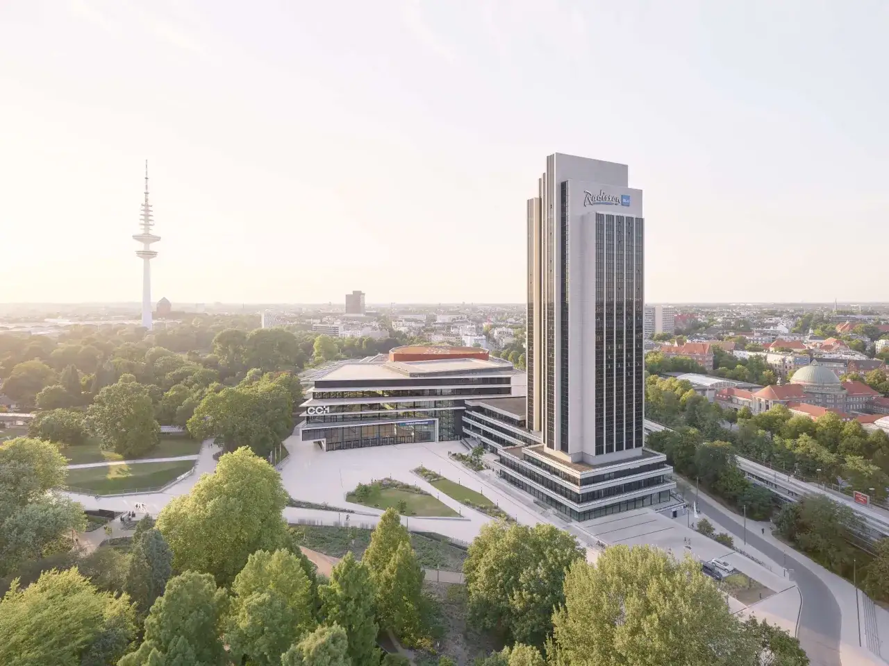 Radisson Blu Hotel w Hamburgu, z charakterystycznym wieżowcem i nowoczesnym budynkiem konferencyjnym, otoczony zielenią i widokiem na miasto.