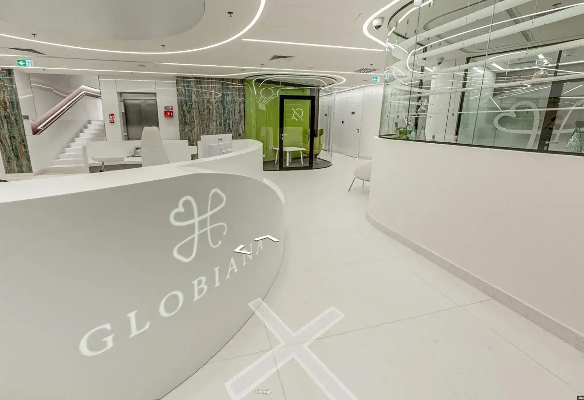 Nowoczesne, białe wnętrze kliniki medycznej z recepcją, schodami i zieloną kapsułą.