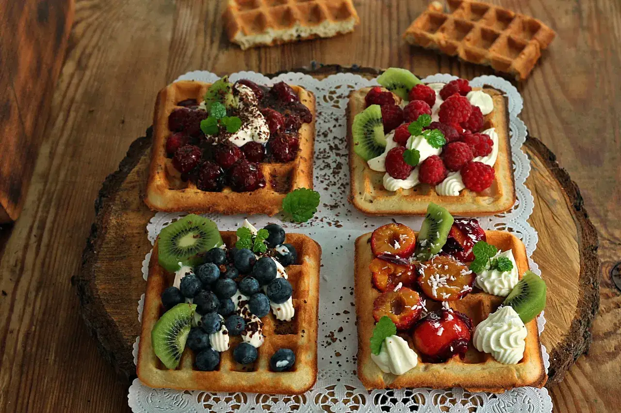 Pyszne gofry belgijskie przepis na deser z owocami: maliny, borówki, kiwi i śliwki z bitą śmietaną.