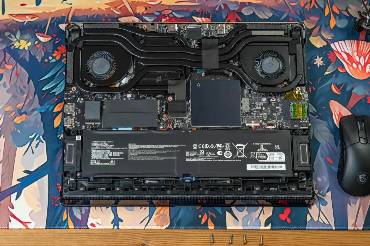 Laptop-Innenleben f&uuml;r ein Upgrade: Akku, L&uuml;fter und Hauptplatine sind sichtbar. Ein Gaming-Maus liegt daneben.