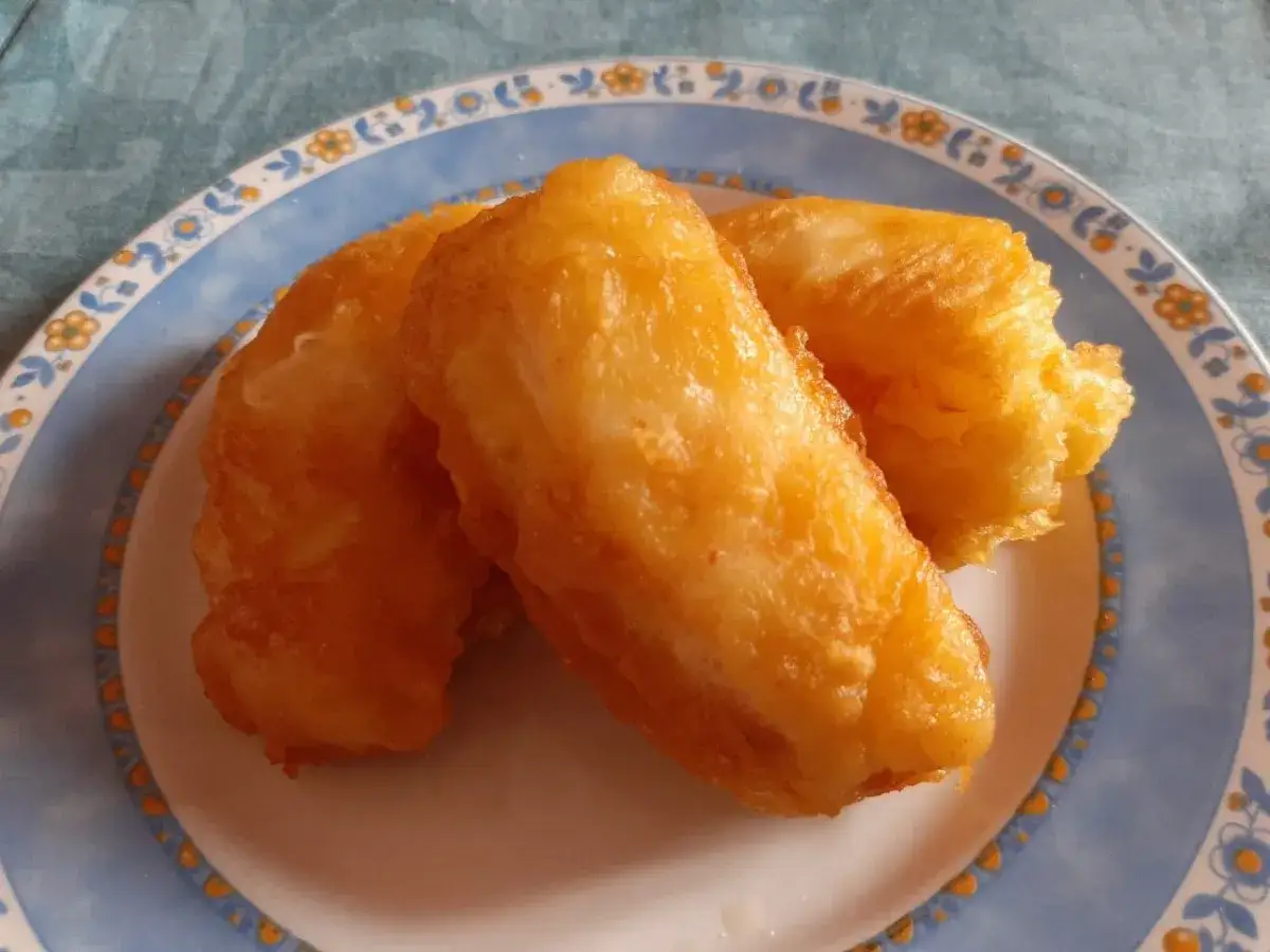 Tres trozos de bacalao rebozado dorados y crujientes, servidos en un plato azul con borde decorado.
