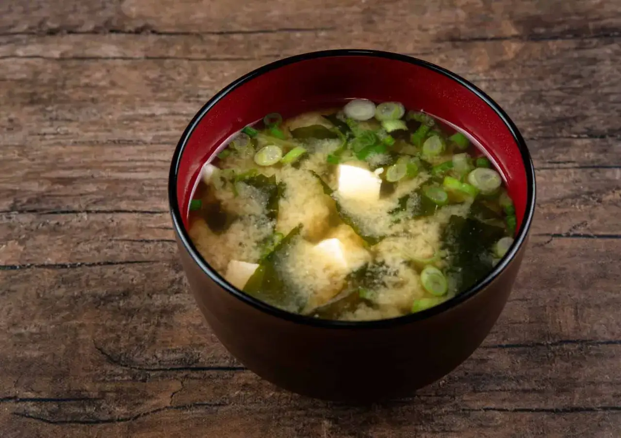 A miska zupy miso z kostkami tofu, wodorostami i szczypiorkiem na drewnianym tle.