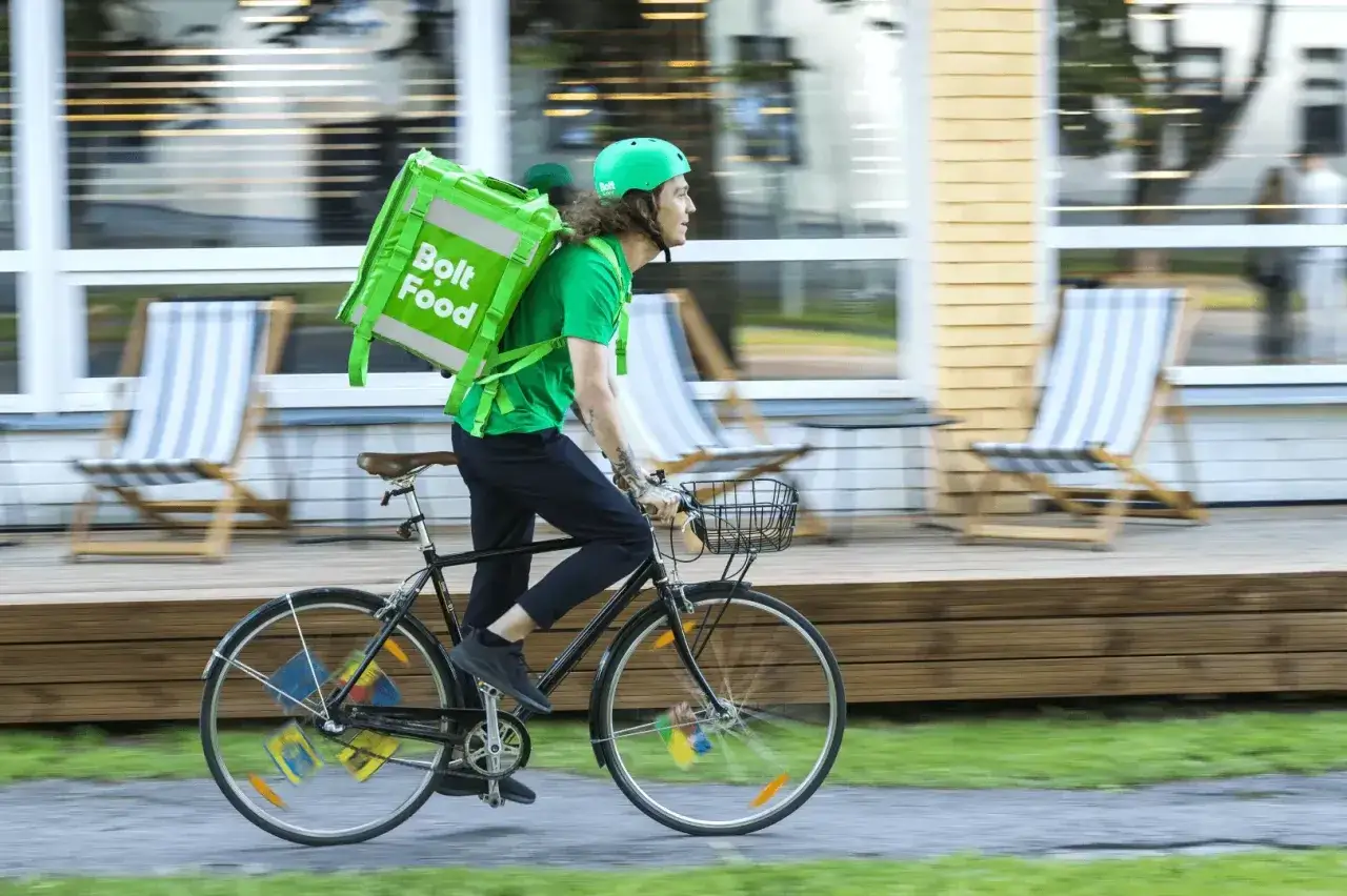 Kurier Bolt Food na rowerze, z zieloną torbą na plecach, pędzi po ulicy. To jego sposób na zarobki.