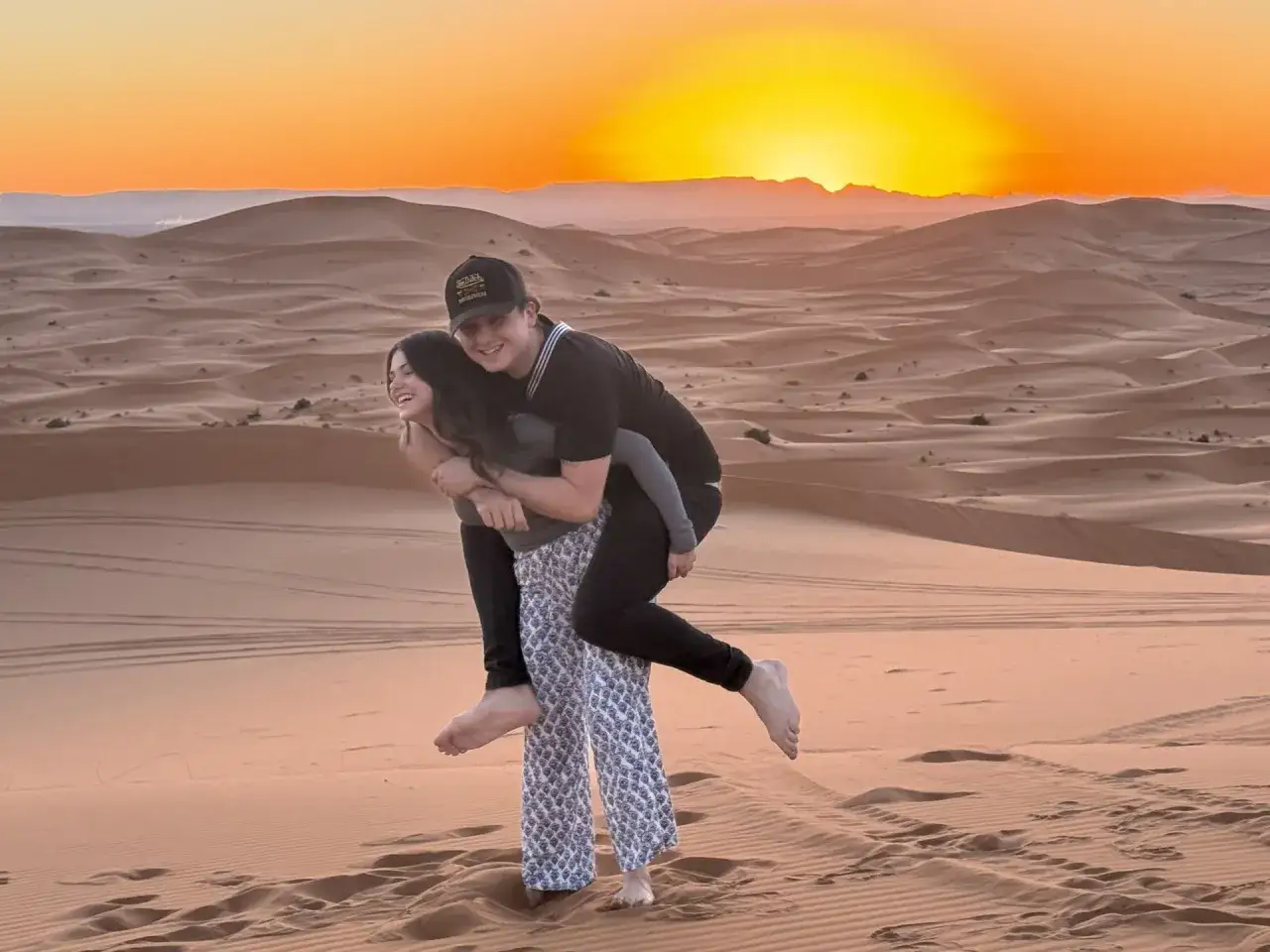 Dos j&oacute;venes disfrutan de un atardecer en las dunas de Marruecos, un recuerdo imborrable de su viaje con ni&ntilde;os.