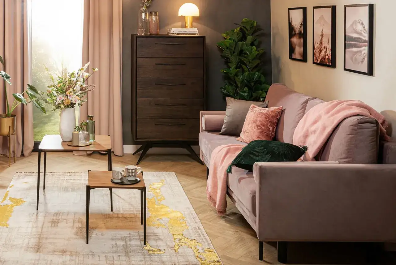Przytulny salon w odcieniach brązu i pudrowego różu. Miękka kanapa, drewniana komoda i stylowe dodatki tworzą ciepłą atmosferę.