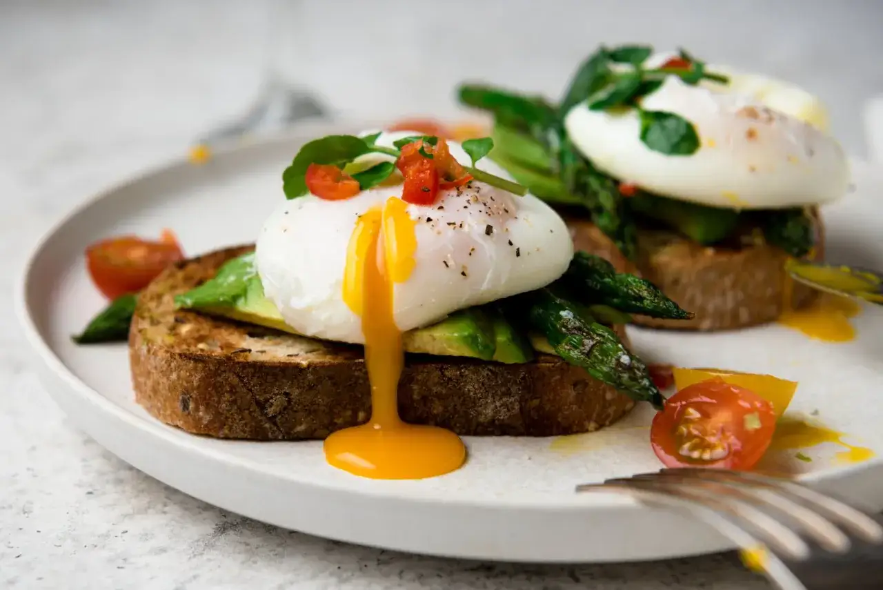 Délicieuse tartine œuf poché sur avocat et asperges, avec des tomates cerises. Le jaune coule, invitant à la dégustation.