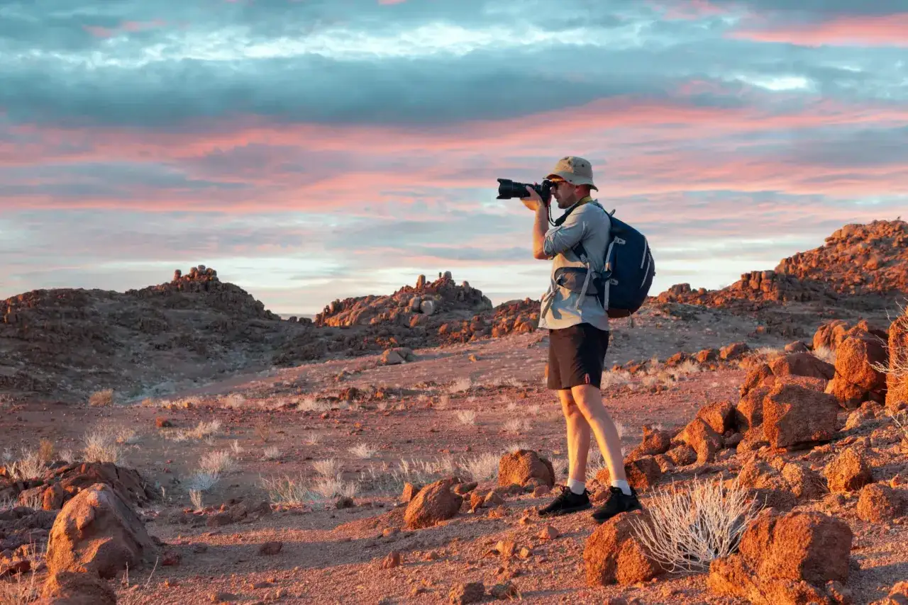 Fotograf w namibijskim krajobrazie o zachodzie słońca. Ceny wycieczek do Namibii mogą być różne, ale widoki są bezcenne.