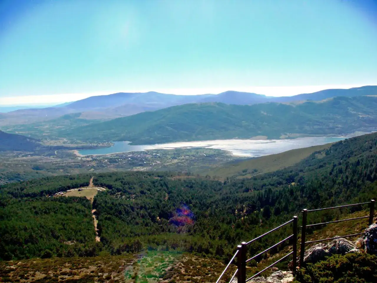 Vista panorámica desde el puerto de Navafría, con un embalse y montañas verdes bajo un cielo azul.