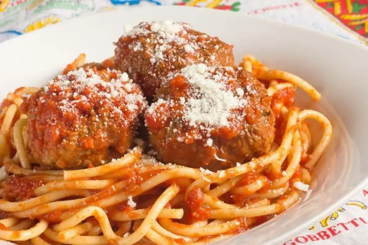 Un plato de spaghetti con tres generosas albóndigas (polpette) cubiertas de salsa de tomate y queso rallado.