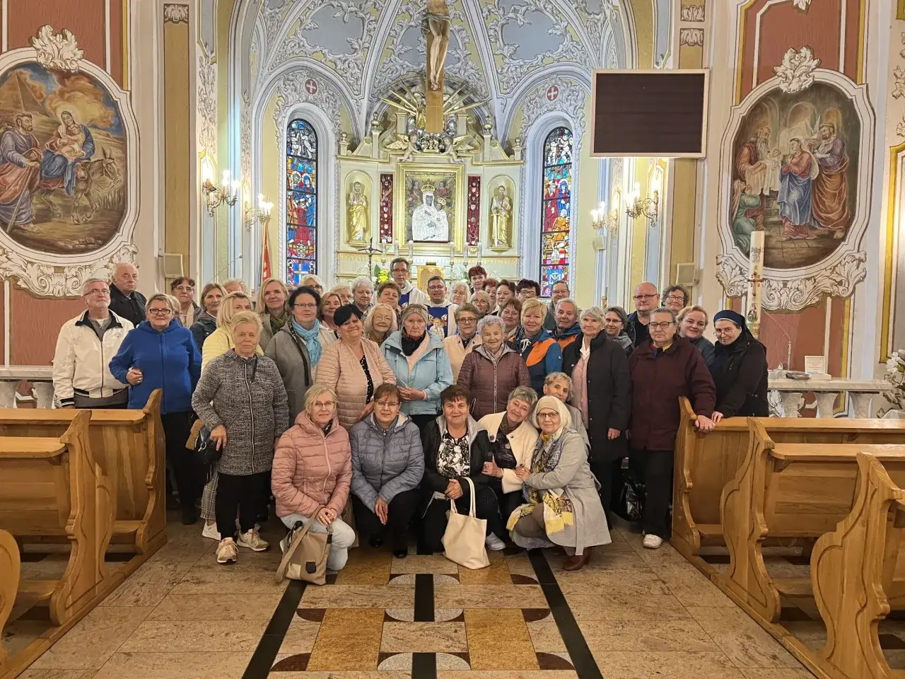 Grupa osób pozuje do zdjęcia w kościele. Różnica między pielgrzymką a wycieczką krajoznawczą do kościołów jest widoczna w ich skupieniu i atmosferze.
