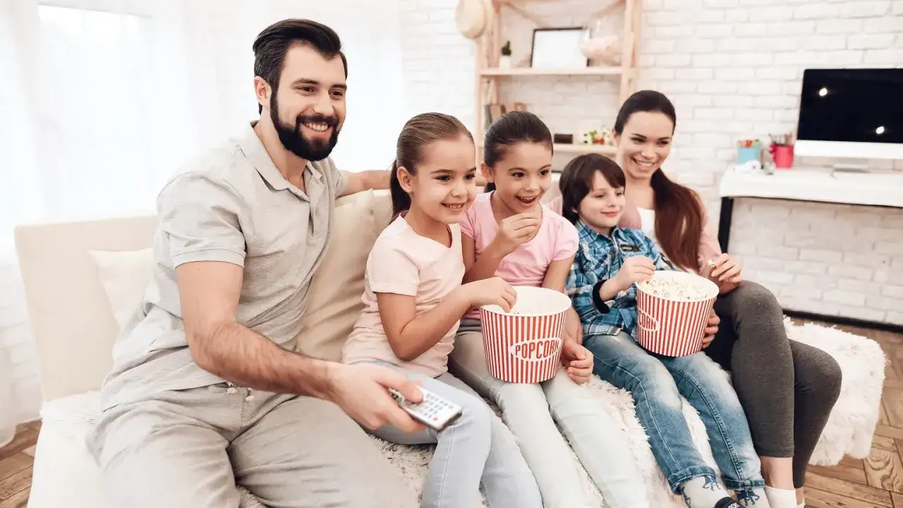 Rodzina ogląda filmy dla dzieci 10-12 lat, zajadając popcorn. Radość na twarzach dzieci i rodziców.