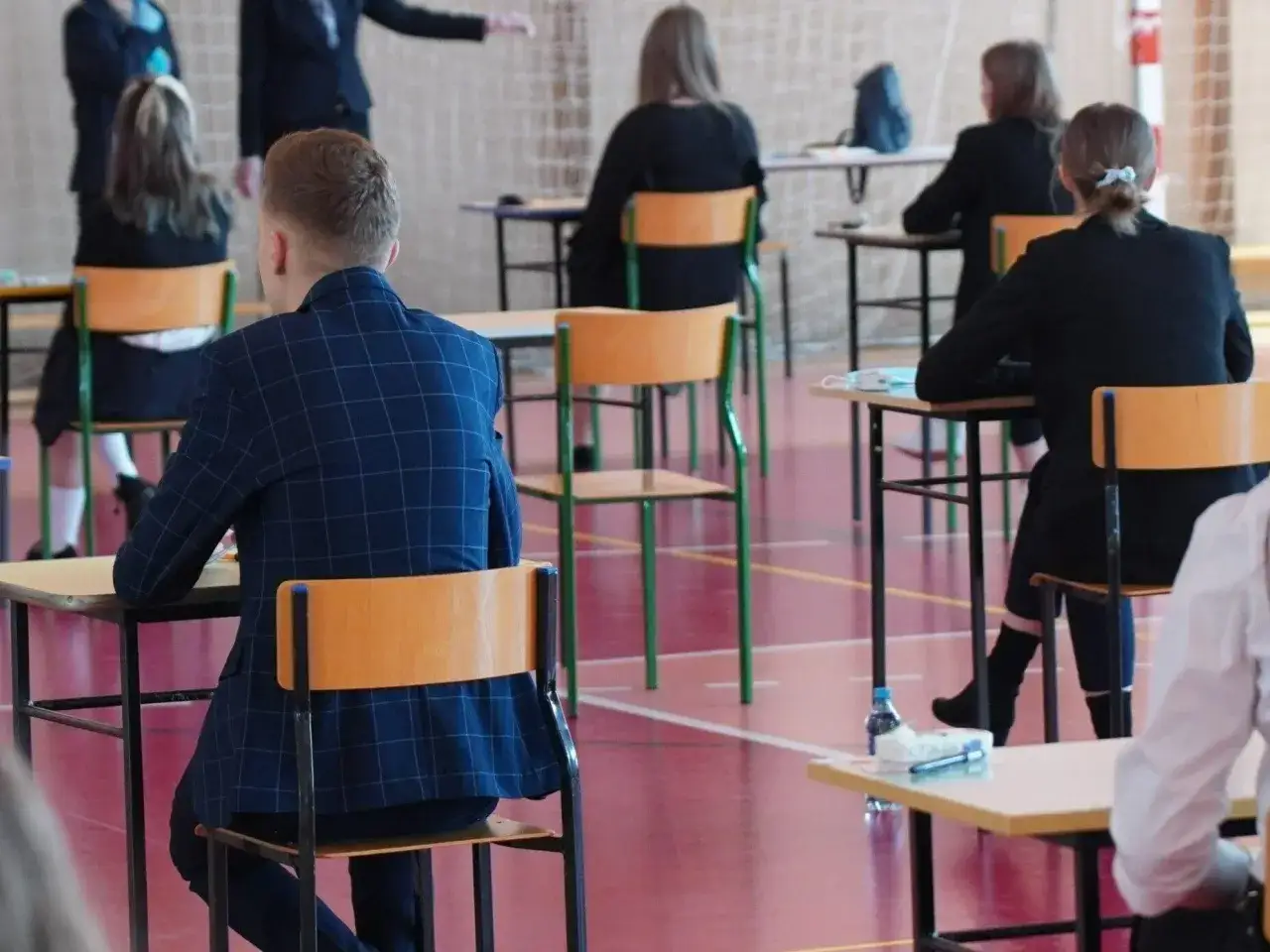Uczniowie siedzą w ławkach, przygotowując się do egzaminu. Wszyscy skupieni, czekają na rozpoczęcie pisania. Wyniki matur już niedługo.