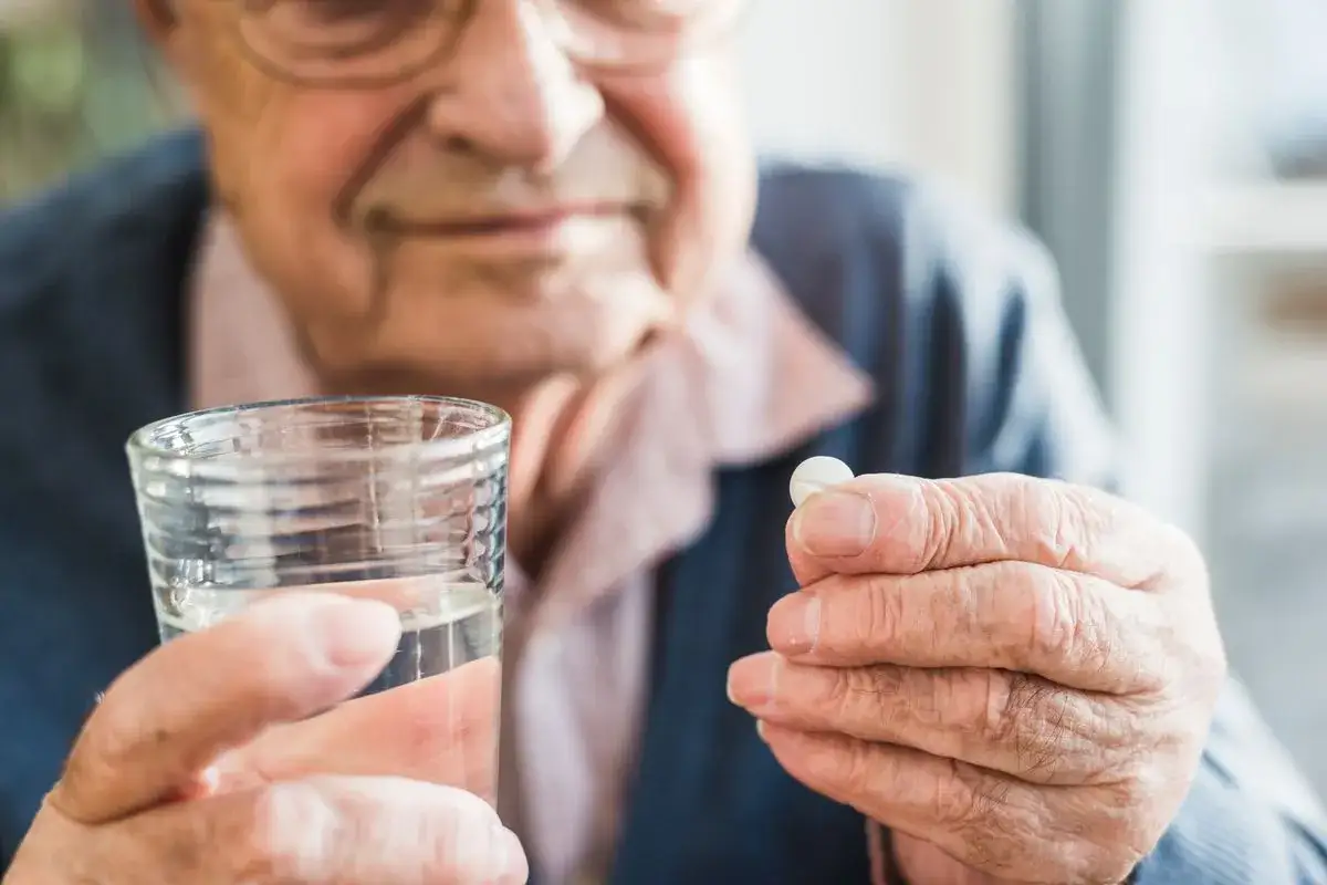 &Auml;lterer Mann h&auml;lt Tablette und Glas Wasser. Wichtig bei kreislaufproblemen bei Hitze: Medikament einnehmen.