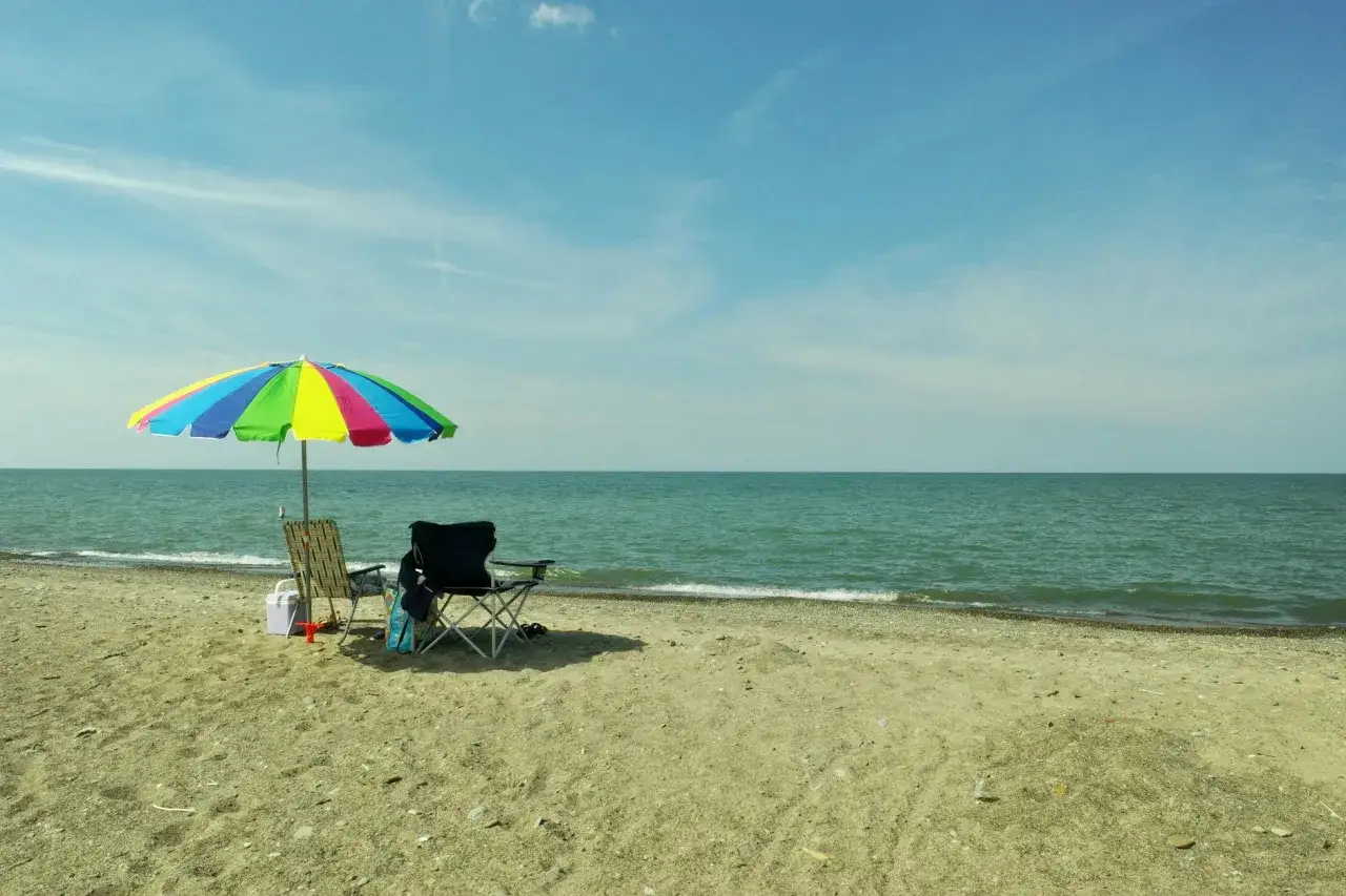 Plaża nad Balatonem, dwa krzesła i parasol. Spokojne wody i piasek. Ceny noclegów nad Balatonem mogą być różne.