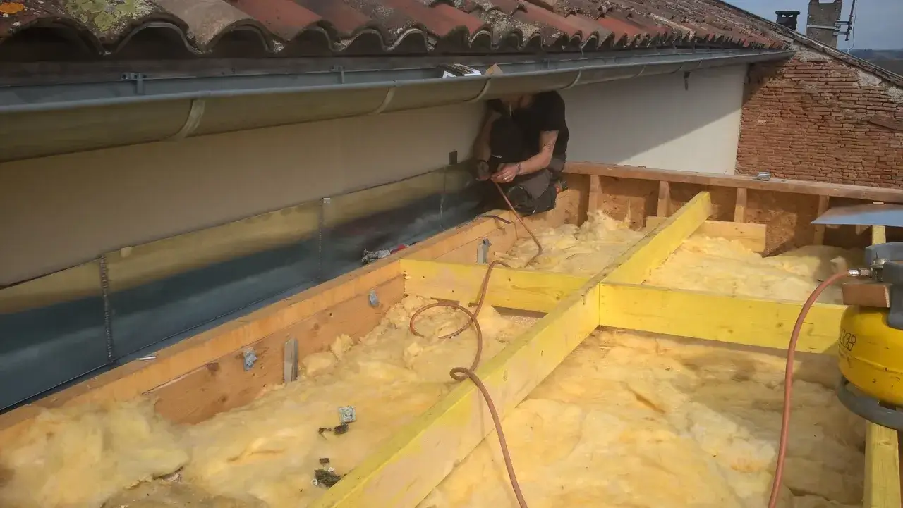 Un ouvrier installe une toiture bac acier isolé. L'isolation jaune est visible sous la structure en bois.