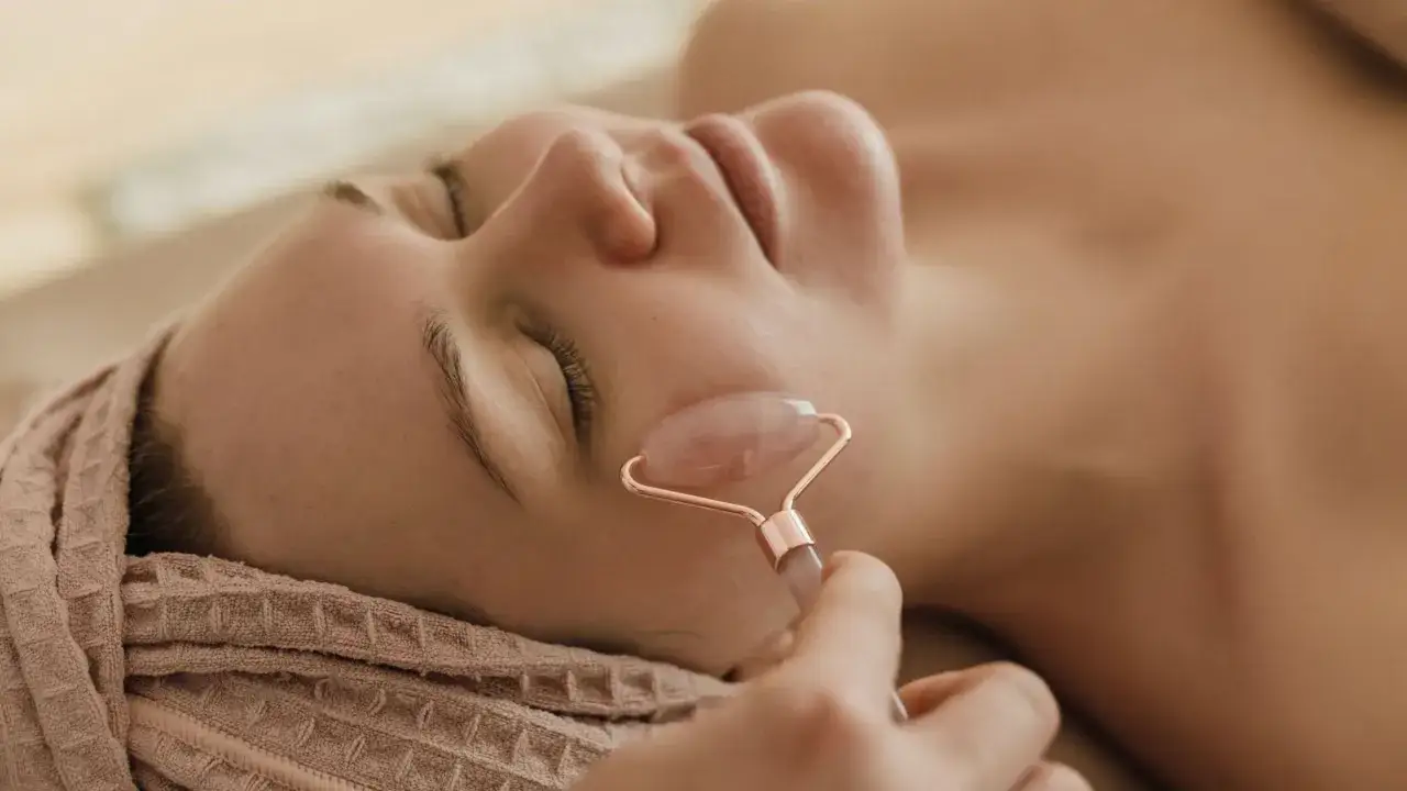 Persona relajada recibe un masaje facial con rodillo de cuarzo rosa, parte de un tratamiento de drenaje linfático facial.