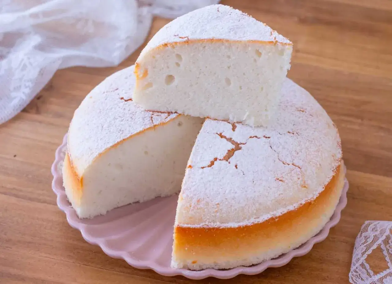 Deliziosa torta senza glutine, soffice e leggera, cosparsa di zucchero a velo su un piatto rosa.