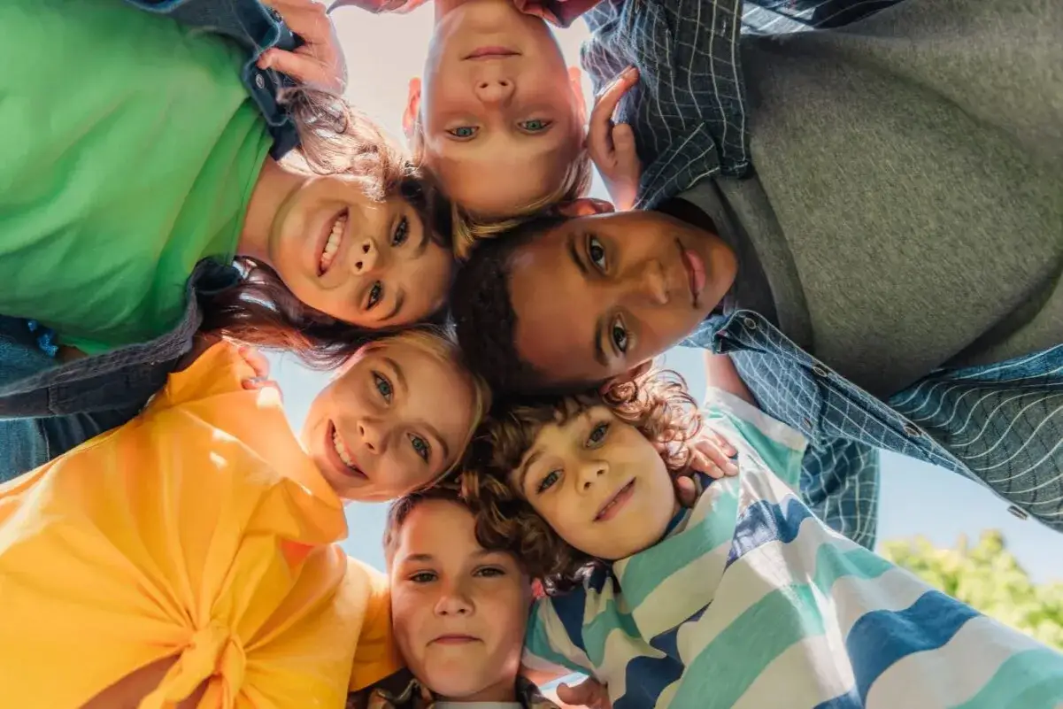Six enfants souriants forment un cercle, leurs visages se rapprochant. Ils semblent heureux et en sécurité, comme dans un centre d'accueil pour mineur.