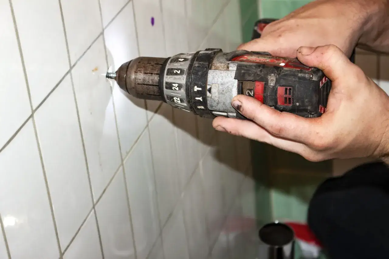Manos sujetando un taladro para taladrar azulejos. Se ve el broca entrando en la pared.