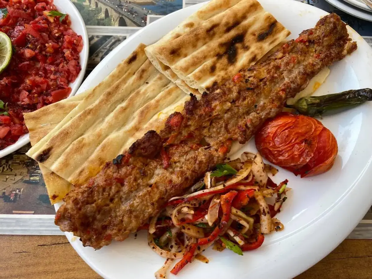 Pyszne tureckie jedzenie: kebab z mięsa mielonego, grillowany pomidor, papryka i świeży chlebek.