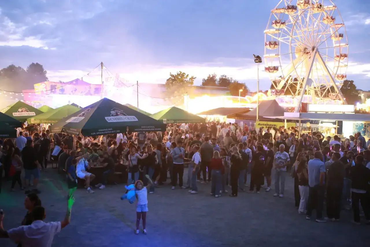 Menschenmenge auf dem Pferdemarkt Beerfelden mit Riesenrad und Bierzelten im Abendlicht.