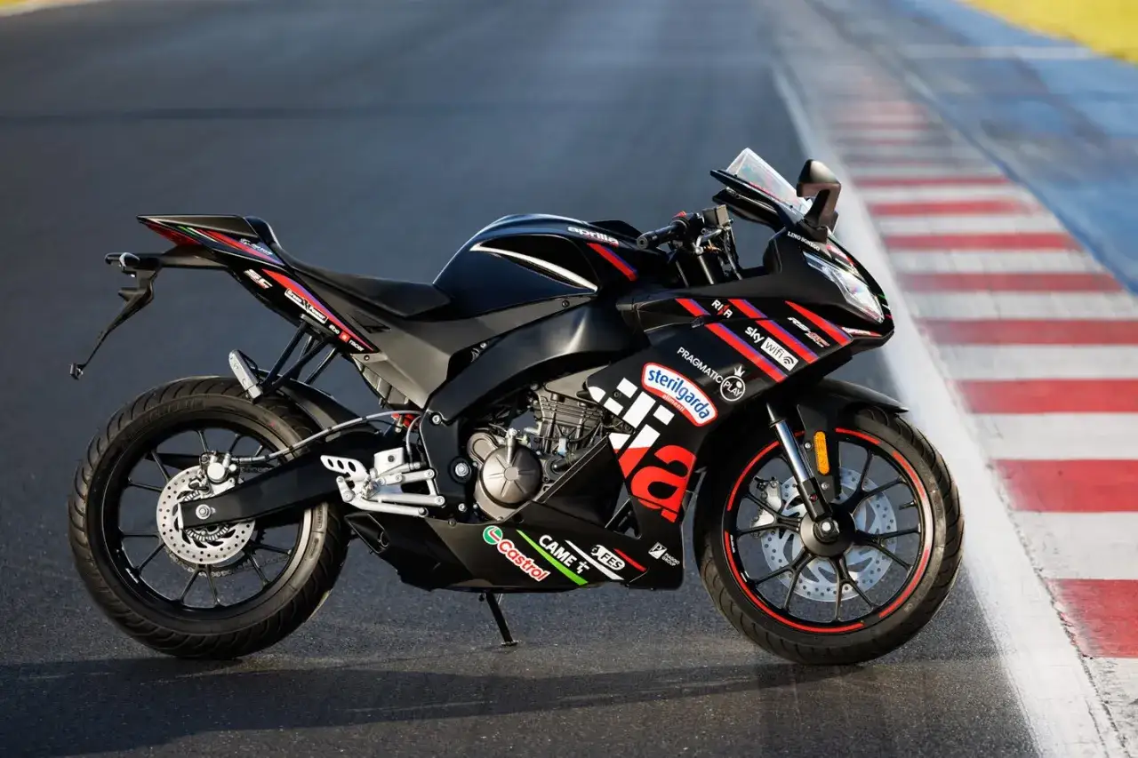 Czarny motocykl Aprilia RS 125 z czerwonymi akcentami na felgach i owiewkach, gotowy do osiągnięcia v-max na torze wyścigowym.