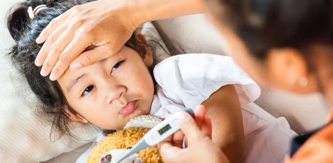 Mama sprawdza, jak mierzyć temperaturę termometrem elektronicznym u chorej córeczki.