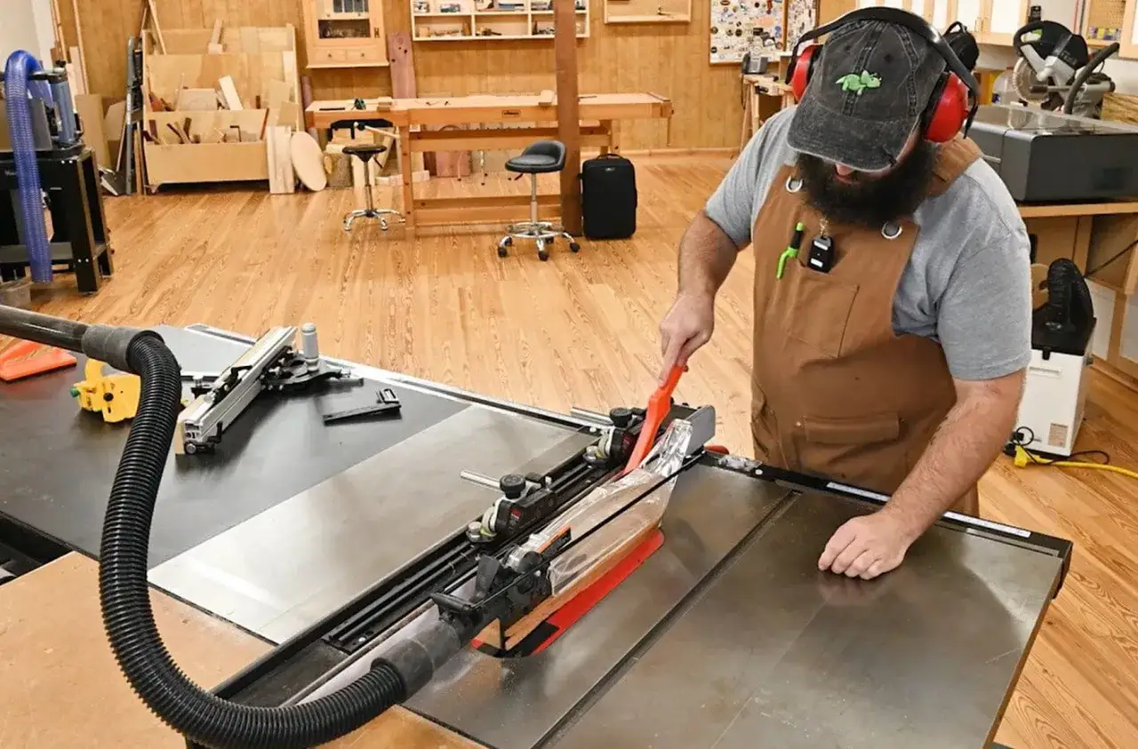 Un artisan utilise un poussoir pour fabriquer une scie sur table, dans un atelier bien rangé.
