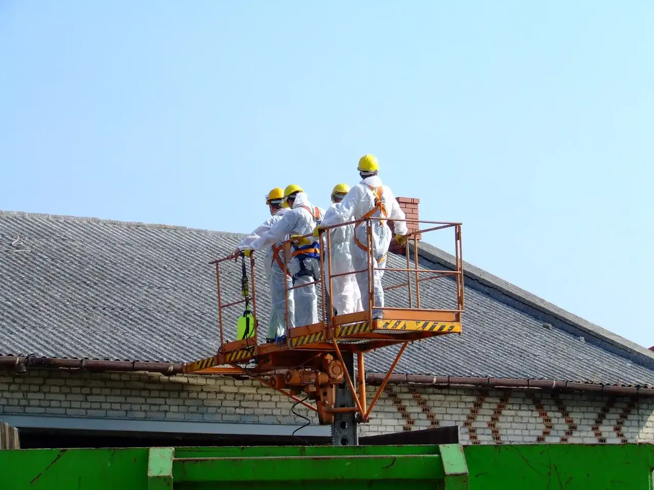 Ekipa w kombinezonach na podnośniku przygotowuje się do prac związanych z wymianą dachu, być może w ramach programu dotacje na wymianę dachu.