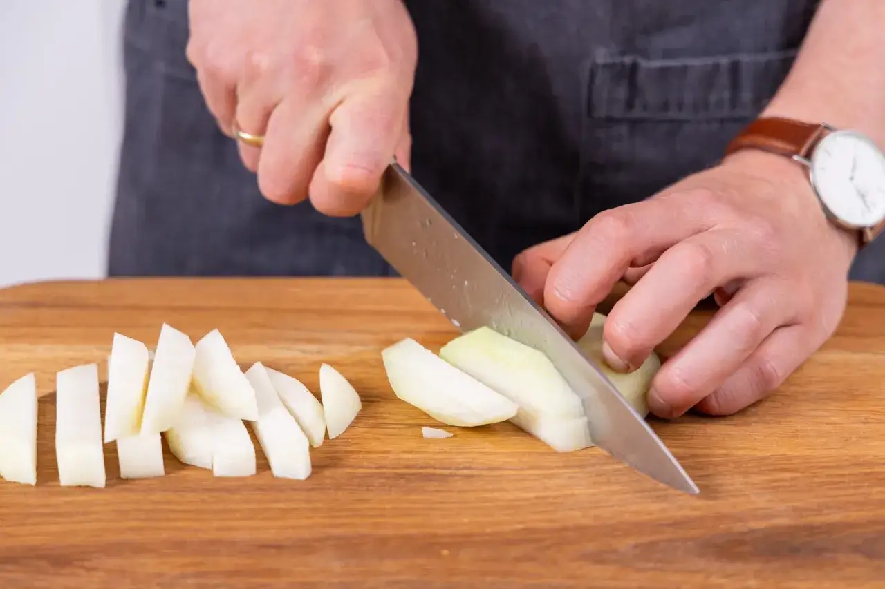 Hände schneiden Kohlrabi in Spalten auf einem Holzbrett. Das Gemüse wird für das Kohlrabi blanchieren vorbereitet.