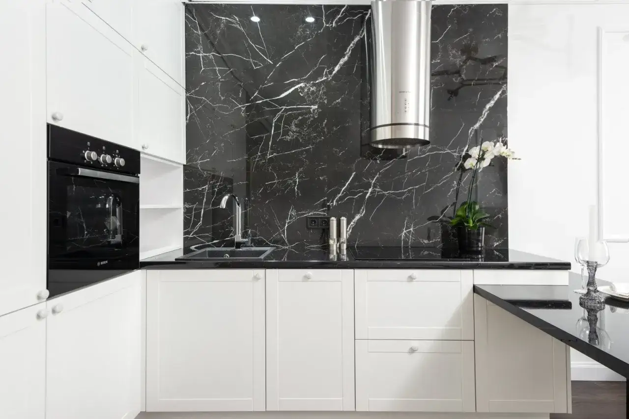 Nowoczesna kuchnia z białymi szafkami i czarnym blatem. Ściana nad blatem ozdobiona płytkami z wzorem **nero marquina**, imitującymi czarny marmur z białymi żyłkami.