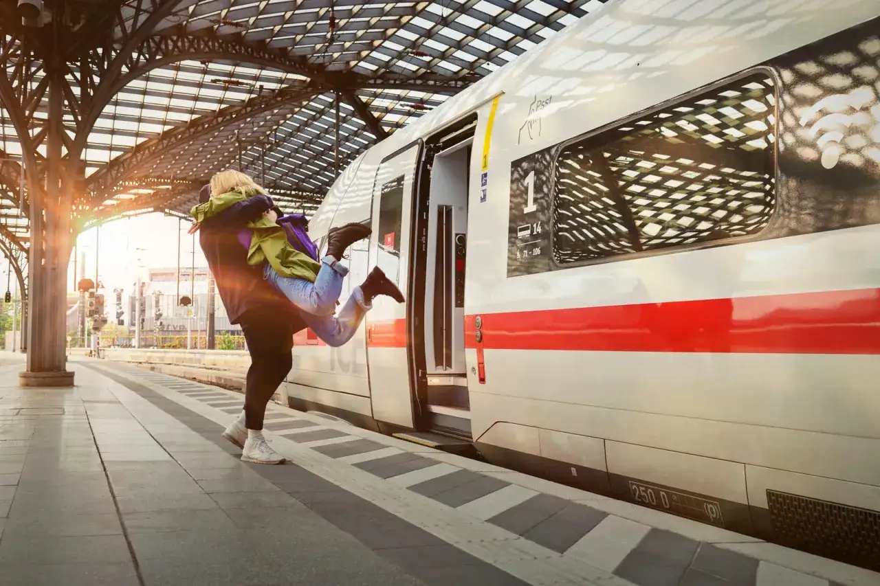 Ein Mann umarmt eine Frau, die er in die Luft hebt, vor einem ICE-Zug am Bahnhof. Der Bahn Fernverkehr beginnt mit einer liebevollen Geste.