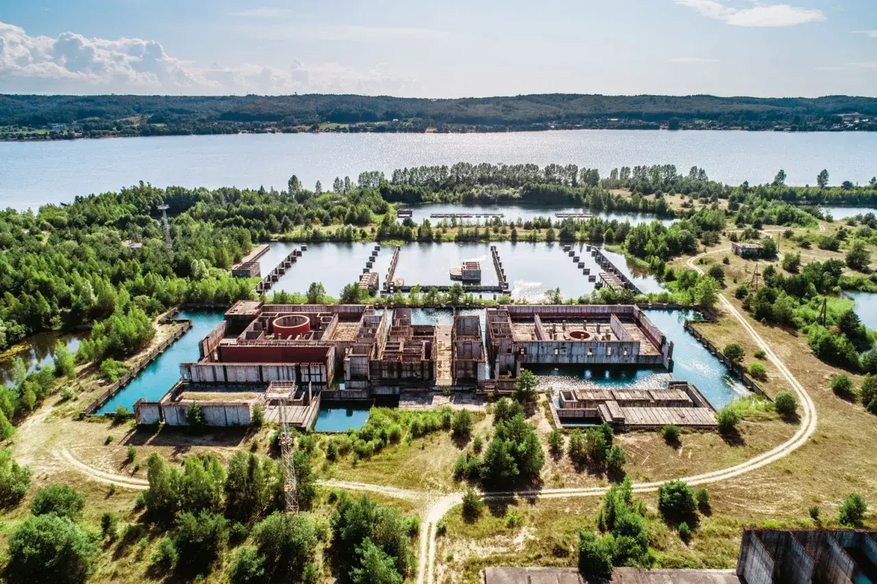 Niedokończona elektrownia w Żarnowcu, otoczona wodą i zielenią, z betonowymi konstrukcjami wznoszącymi się nad zbiornikiem.