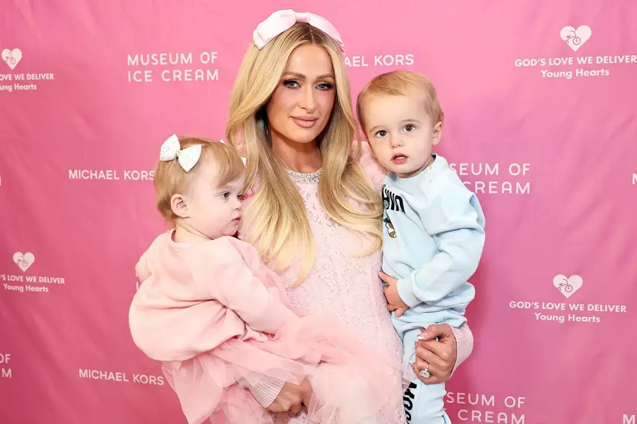 Paris Hilton z dwójką swoich uroczych dzieci, synkiem i córeczką, na tle różowego banera.