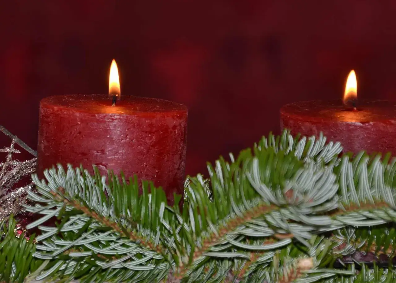 Zwei brennende rote Kerzen auf Tannenzweigen. Der zweite Adventssonntag ist da und bringt Licht in die Dunkelheit.