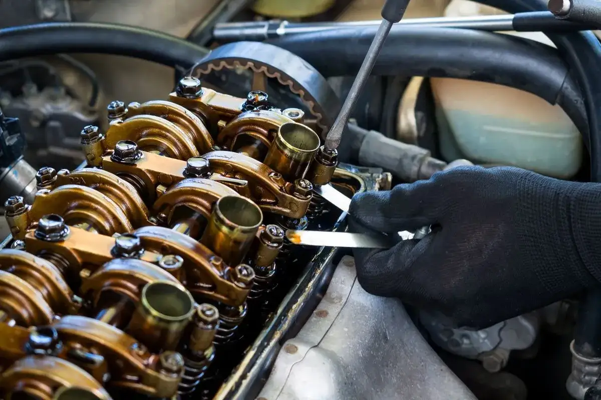 Mechanik w czarnej rękawiczce dokonuje regulacji zawor&oacute;w w silniku samochodowym, co jest kluczowym etapem regeneracji.