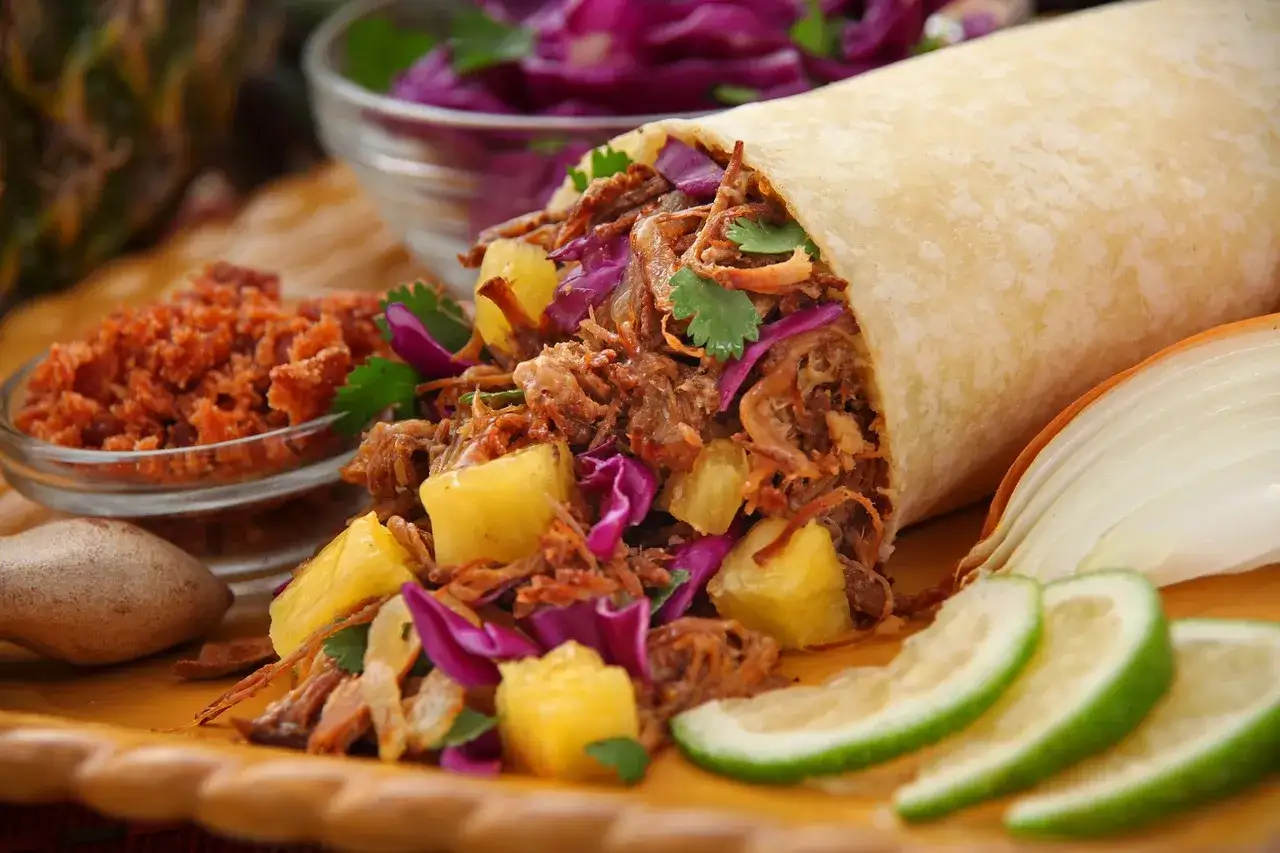 Pyszne dania meksykańskie: burrito z szarpaną wieprzowiną, ananasem i czerwoną kapustą, podane z limonką i salsą.