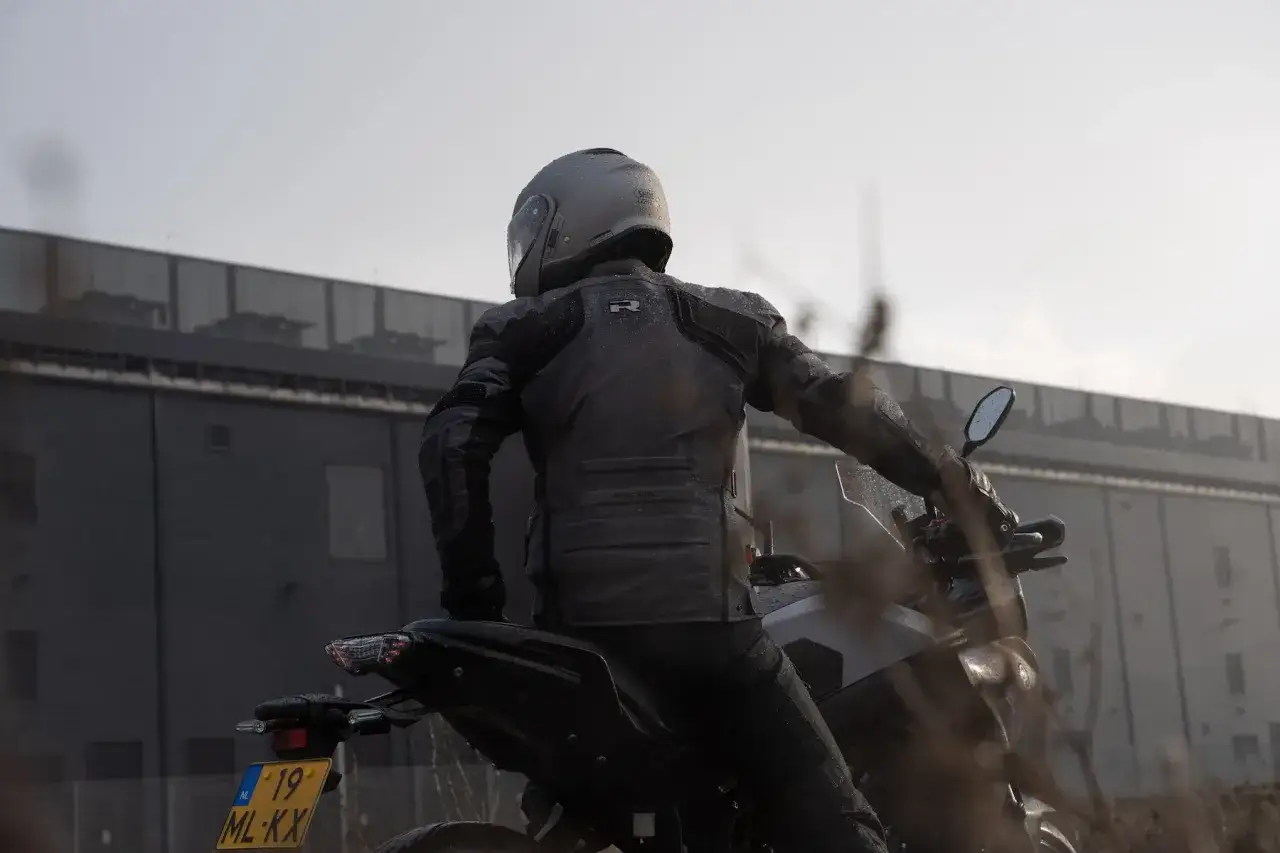 Motociclista con chaqueta impermeable, comparando la protección OutDry vs Gore-Tex en un día lluvioso.