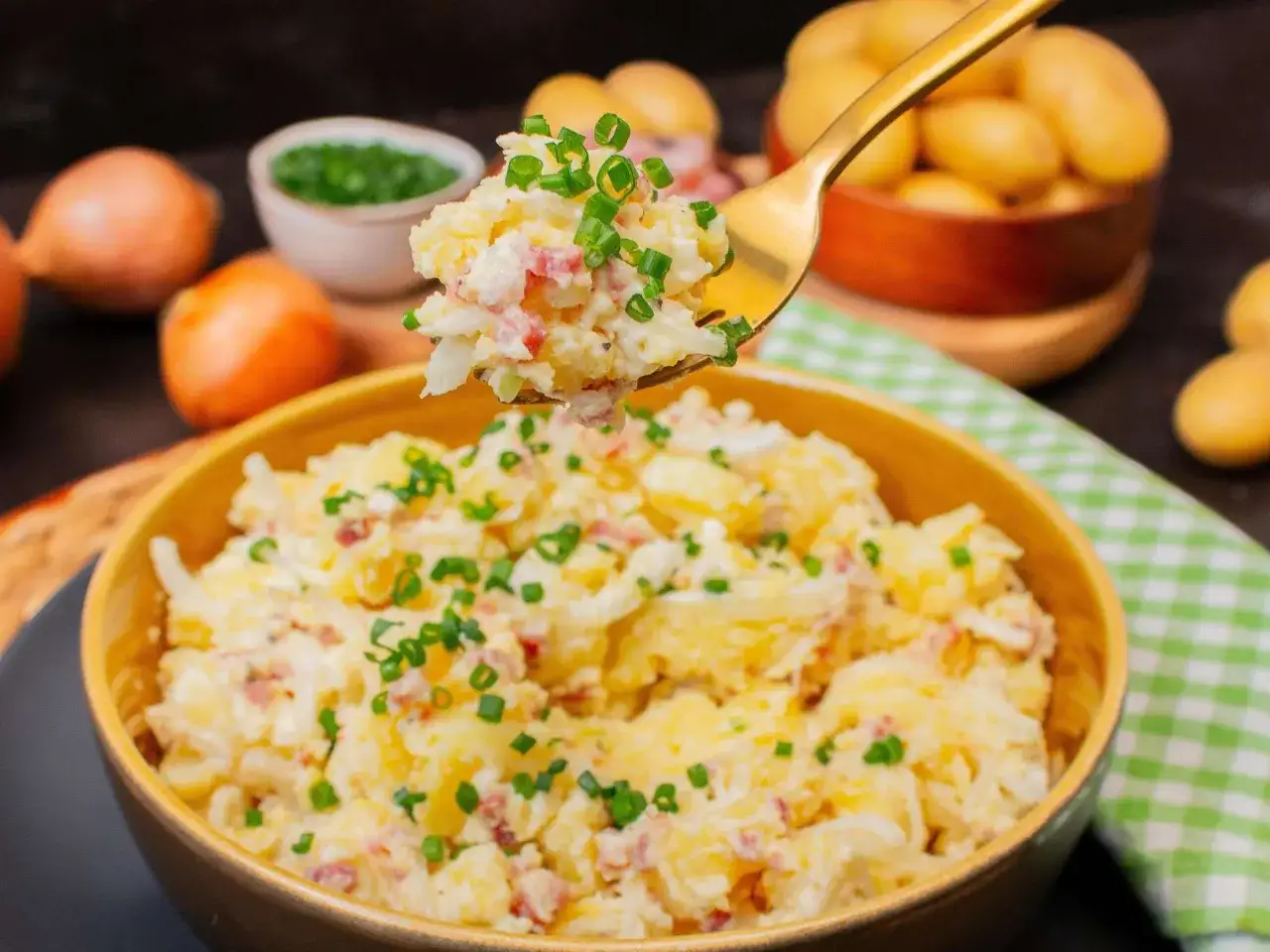 Herzhaftes Kartoffelsalat-Essen im Sommer, garniert mit Schnittlauch. Dazu frische Kartoffeln und Zwiebeln.