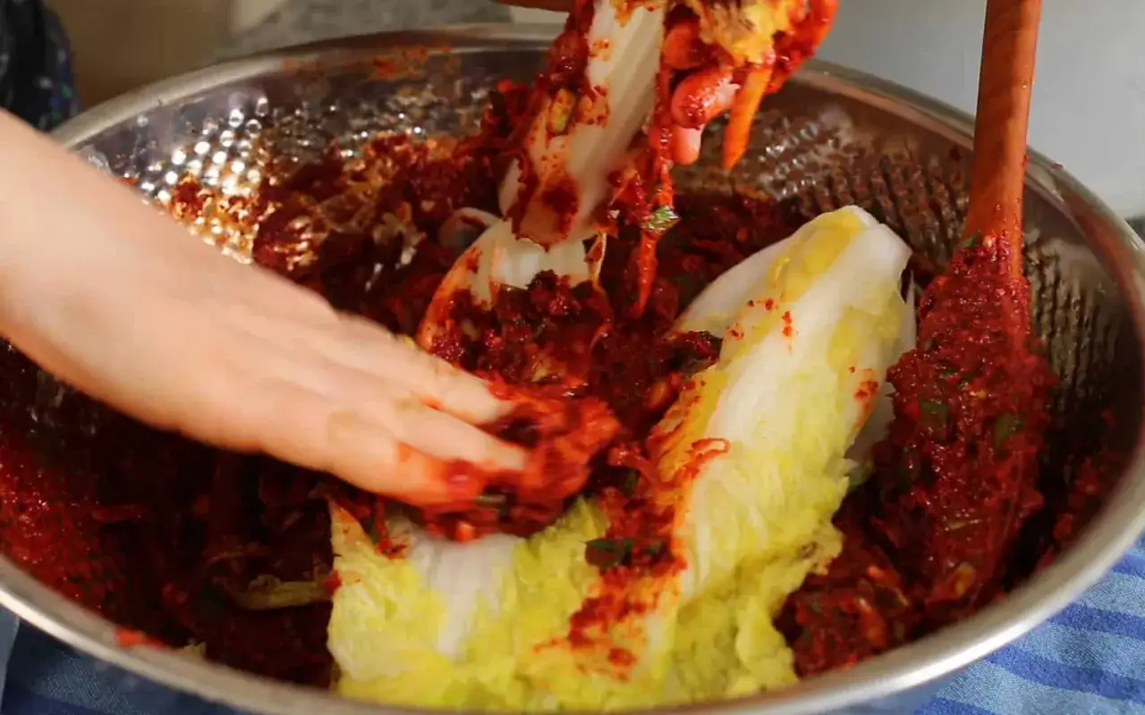 H&auml;nder som arbetar med kinak&aring;l och en kryddig r&ouml;d pasta i en sk&aring;l, f&ouml;rbereder ett kimchi recept.
