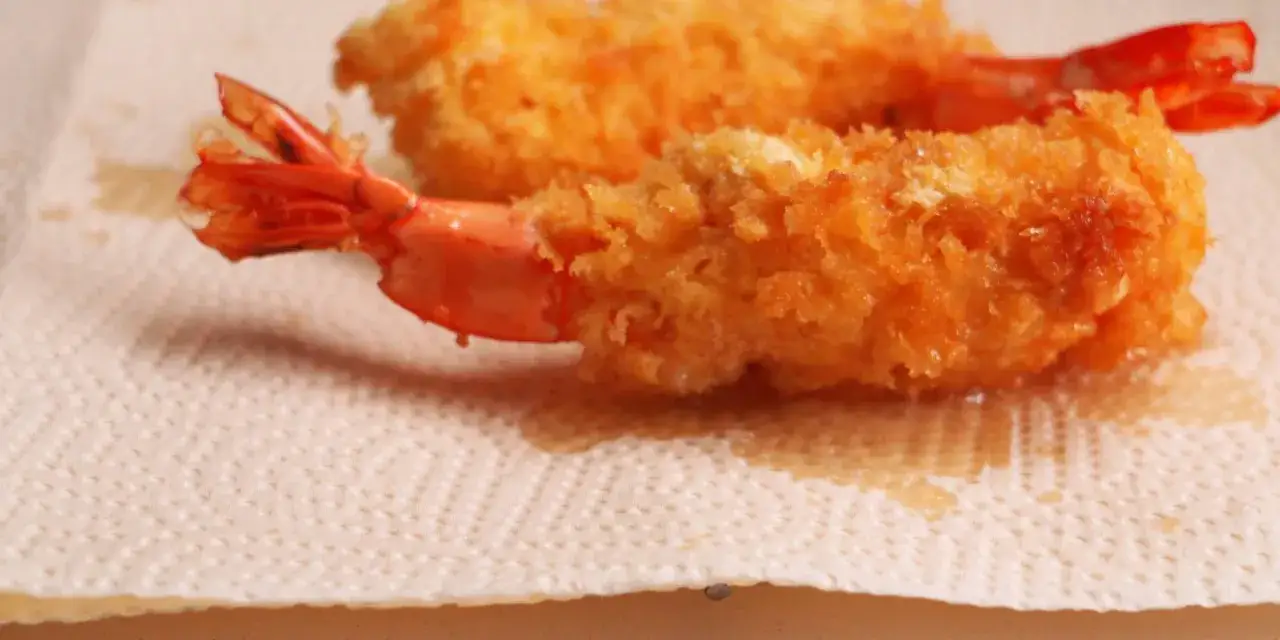 Two golden-brown, crispy japanese fried shrimp rest on a textured paper towel, their tails peeking out.