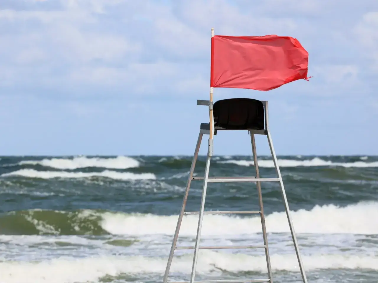 Czerwona flaga na wieży ratownika ostrzega przed niebezpiecznymi warunkami na morzu. Zamknięte plaże Bałtyk, fale i wiatr.