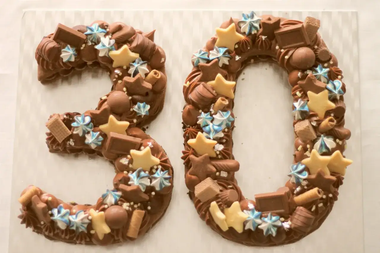 Torta numero cioccolato a forma di 30, decorata con stelle, meringhe e cioccolatini.